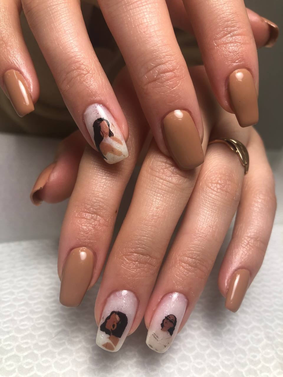 Dłonie z brązowymi, kwadratowymi paznokciami; na dwóch paznokciach portrety kobiet na białym, błyszczącym tle.