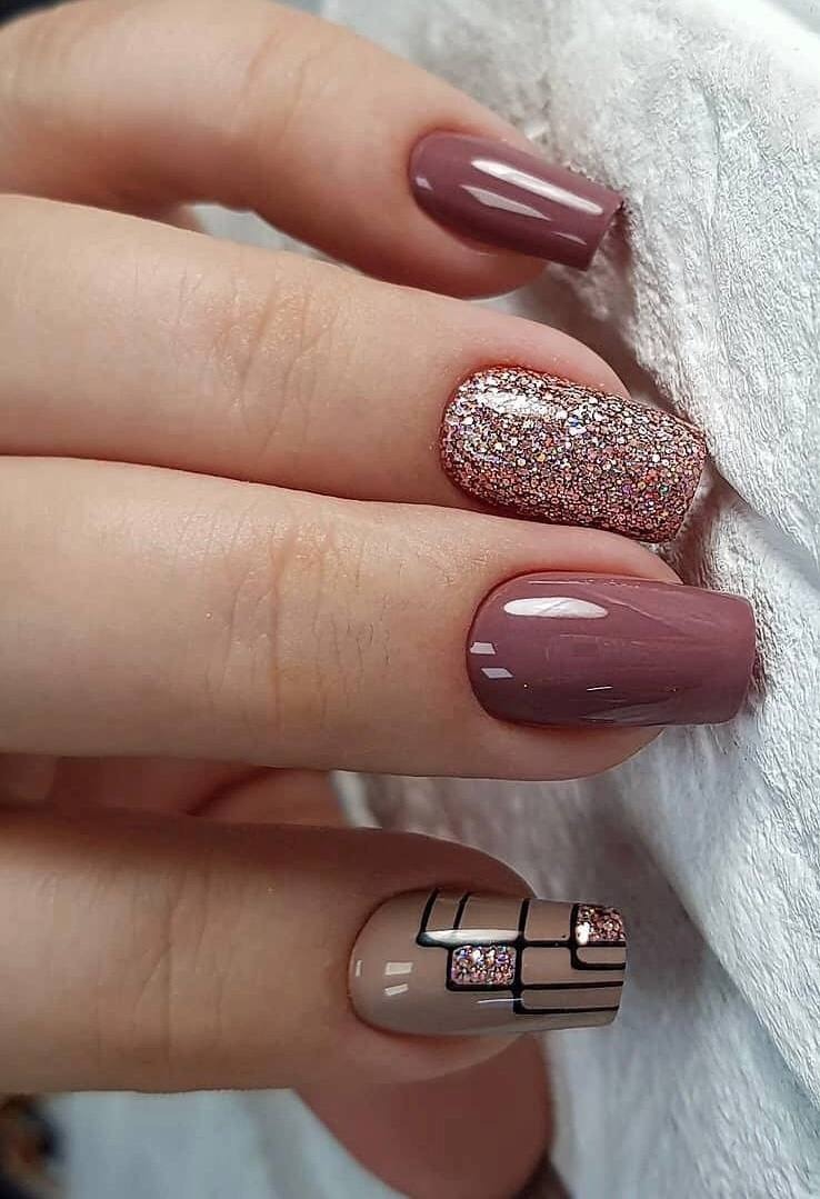 Krótkie paznokcie w odcieniach brązu i beżu, jeden z brokatem, a jeden z geometrycznym wzorem na beżowym tle, wykonane na tle białego ręcznika.