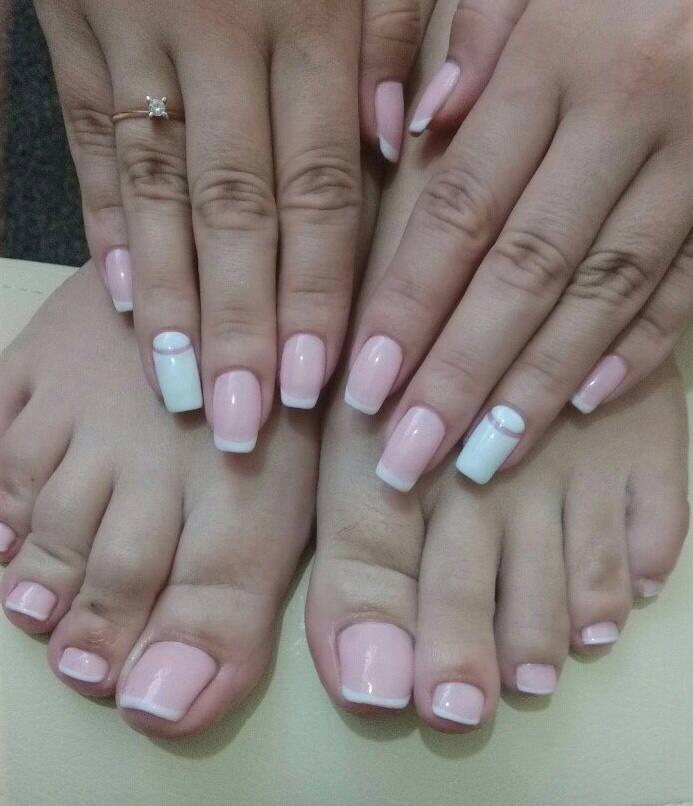 Dłonie i stopy z jasnoróżowym french manicure, jeden paznokieć u dłoni pomalowany na biało z poziomym paskiem, pierścionek z brylantem na palcu dłoni.