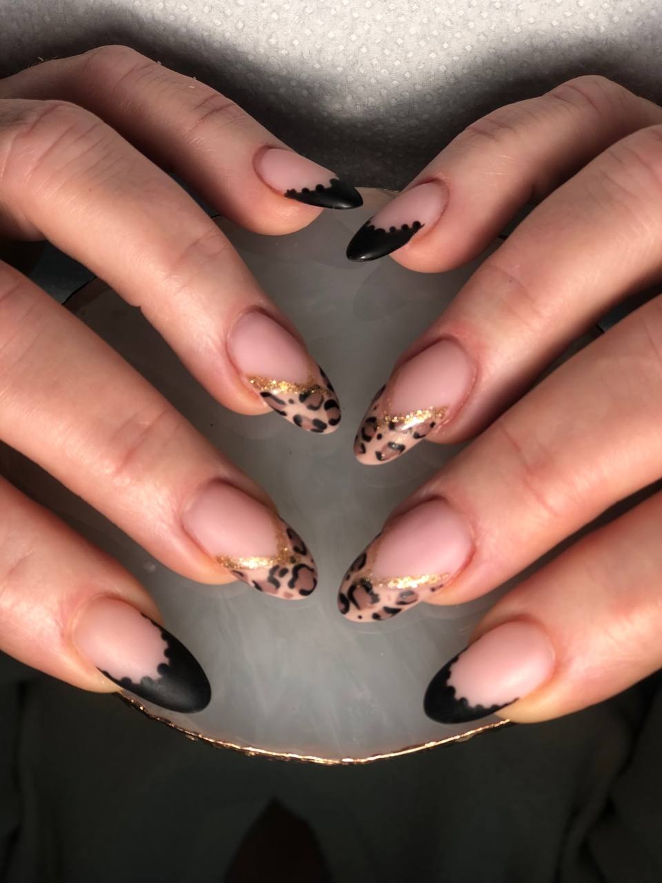 Dłonie z hybrydowymi paznokciami: dwa z panterkowym wzorem i złotym paskiem, dwa z czarną, falowaną końcówką.