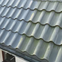 Częściowo oczyszczony dach z szarej dach&oacute;wki ceramicznej, widoczna wyraźna r&oacute;żnica między umytą a zabrudzoną powierzchnią, obok okno dachowe i orynnowanie.