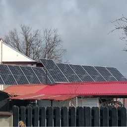 ELEKTROINSTAL Krzysztof Staszewski-Energia odnawialna - Instalacja fotowoltaiczna na dachu domu jednorodzinnego z czerwoną dachówką, widoczna antena telewizyjna na tle pochmurnego nieba.