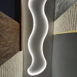 Falisty, podświetlany element dekoracyjny na szarym suficie, widoczne fragmenty wykończenia ścian: imitacja cegły i ciemnoszara farba.