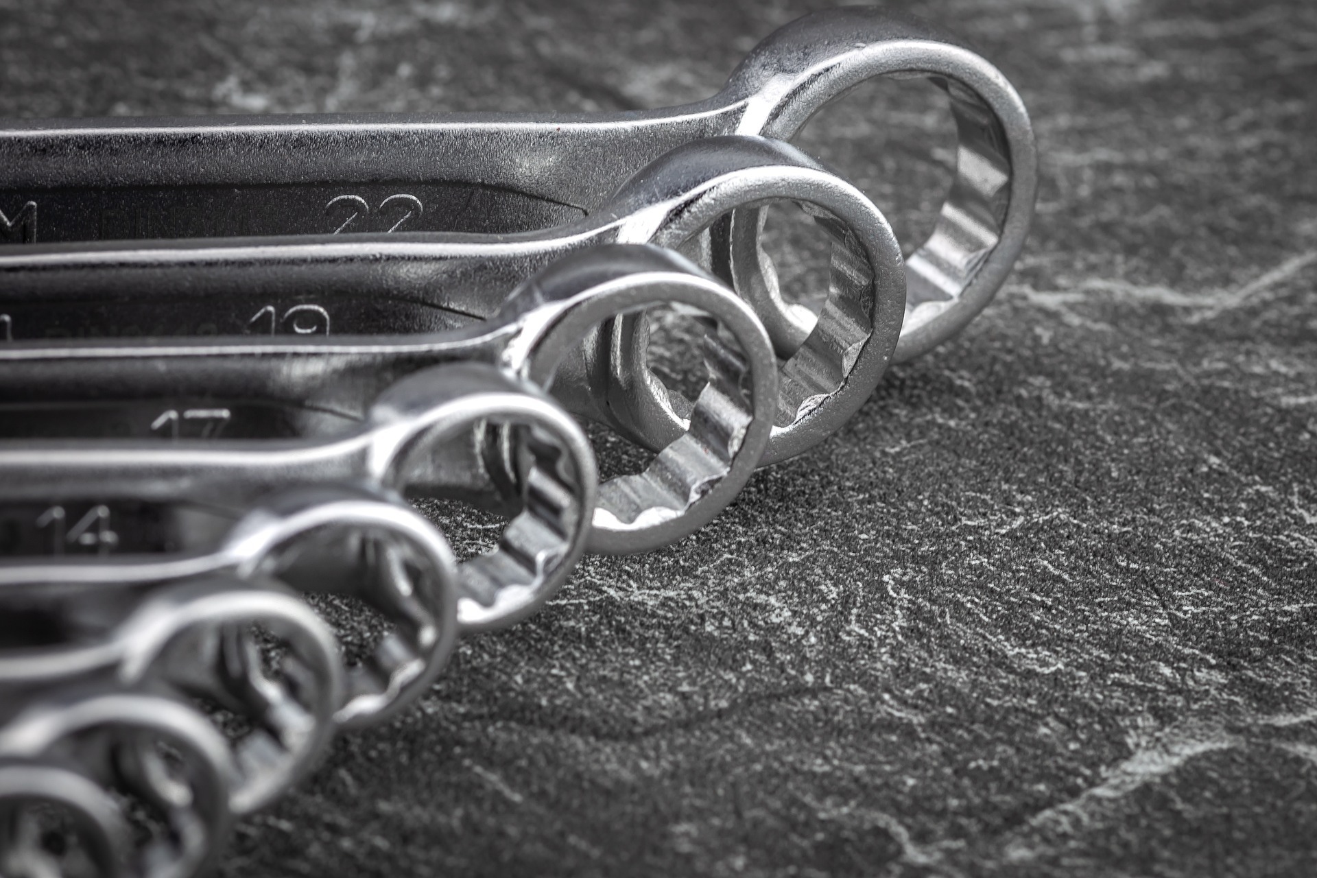 Zestaw kluczy płasko-oczkowych o różnych rozmiarach (14, 17, 19, 22) ułożonych jeden za drugim na szarej, teksturowanej powierzchni, widok z góry pod kątem.