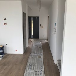 Marcin S. - Przygotowanie do malowania wnętrza: zabezpieczona podłoga, świeżo pomalowane ściany, puszki z farbą Dulux. Widoczne niedokończone otwory na gniazdka elektryczne i wystające kable.