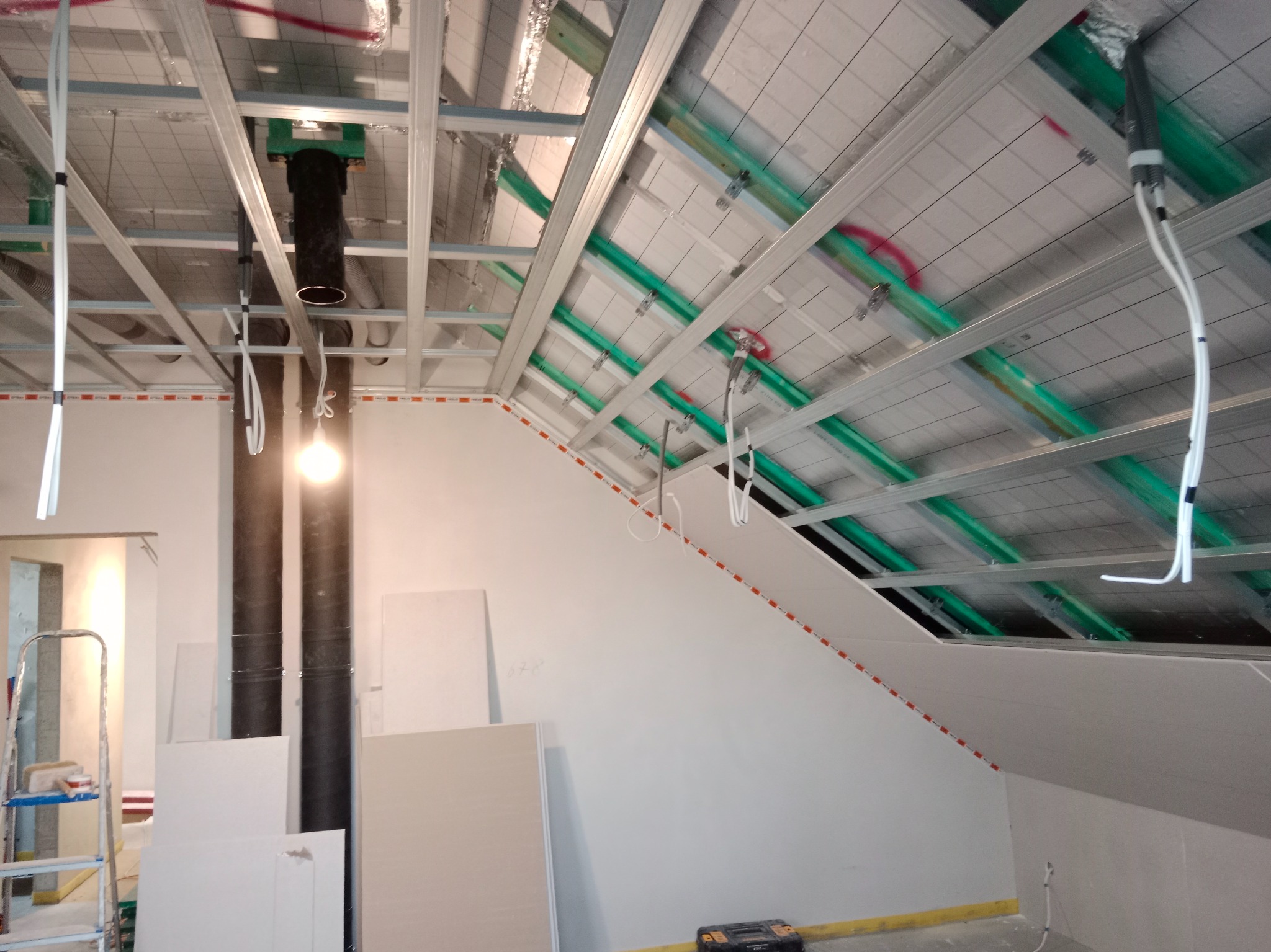 Skośne poddasze w trakcie wykańczania płytami gipsowo-kartonowymi. Widoczne metalowe profile, instalacje i częściowo zamontowane płyty. Prace wykończeniowe w toku.