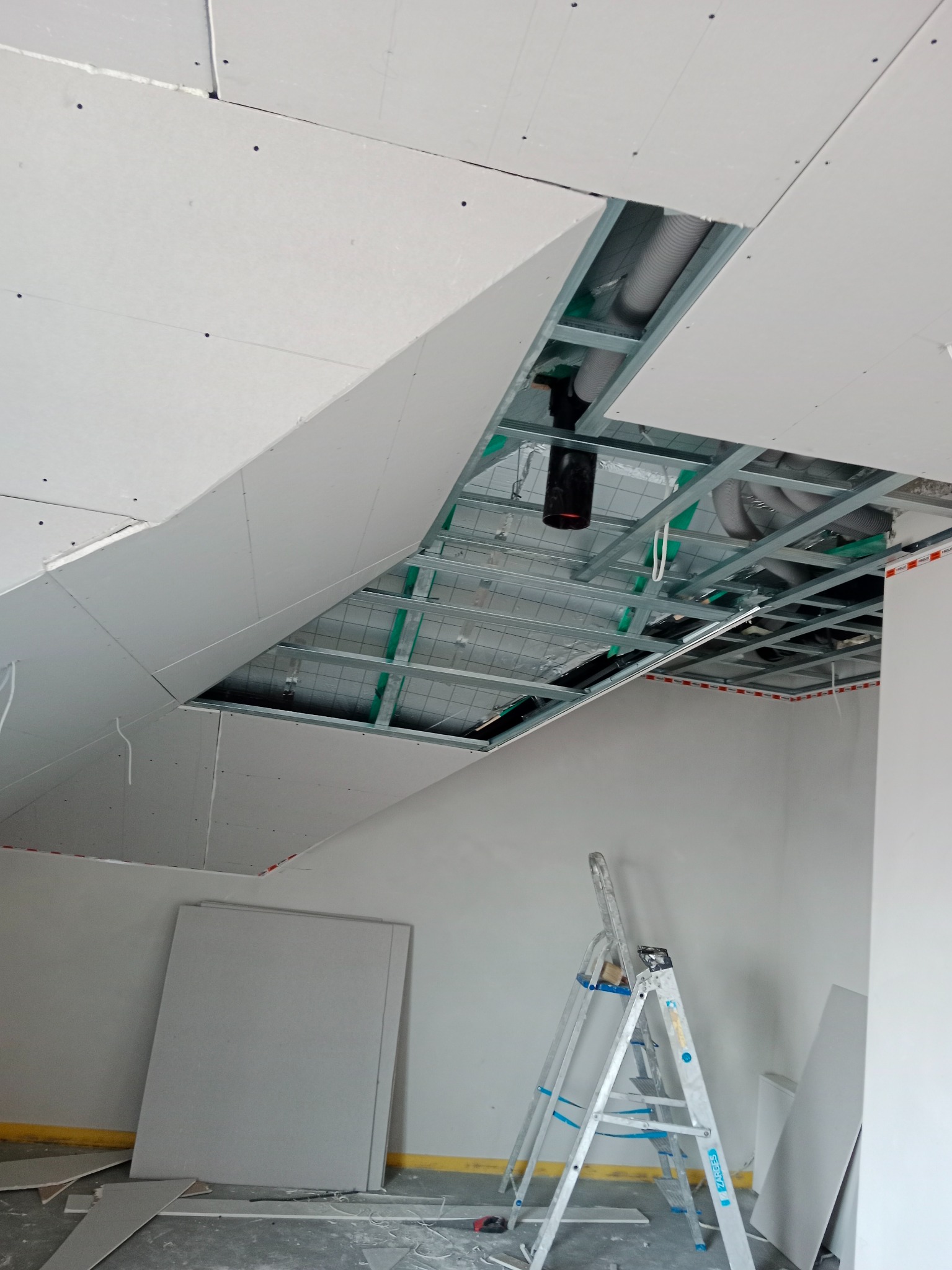 Montaż sufitu podwieszanego z płyt gipsowych w Świerzowej Polskiej. Widoczne profile, instalacja wentylacyjna i drabina. Etap prac wykończeniowych.