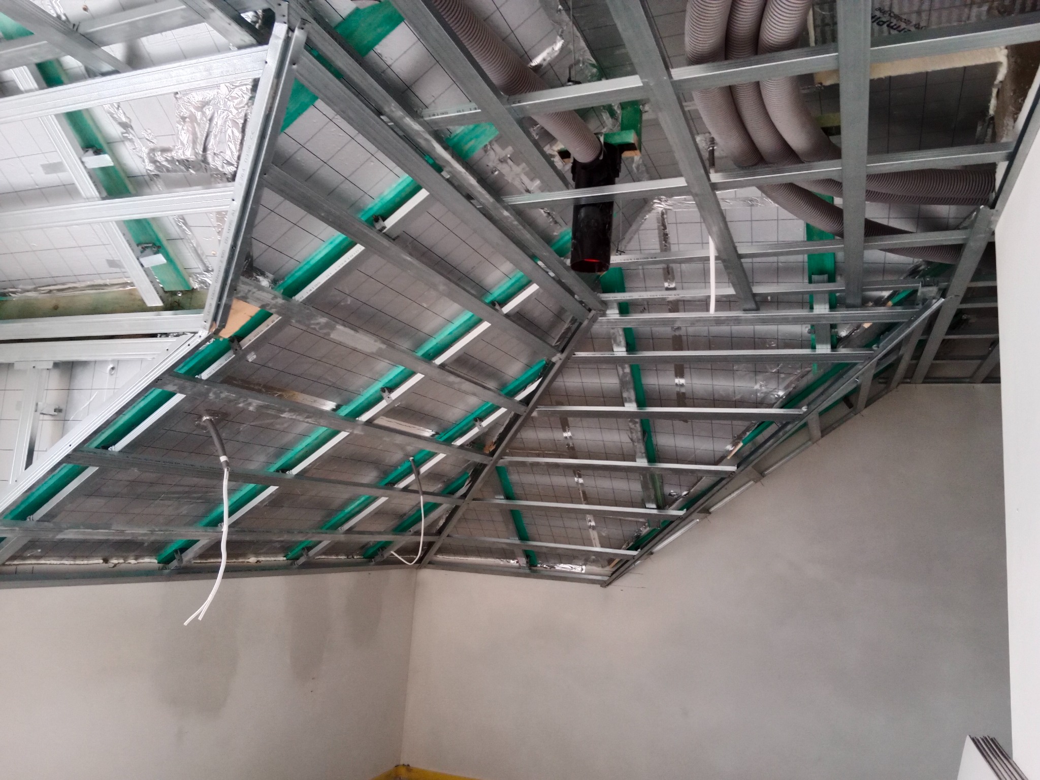 Szkielet podwieszanego sufitu z metalowych profili, widoczne ocieplenie i instalacje wentylacyjne w przestrzeni poddasza. Etap prac wykończeniowych.