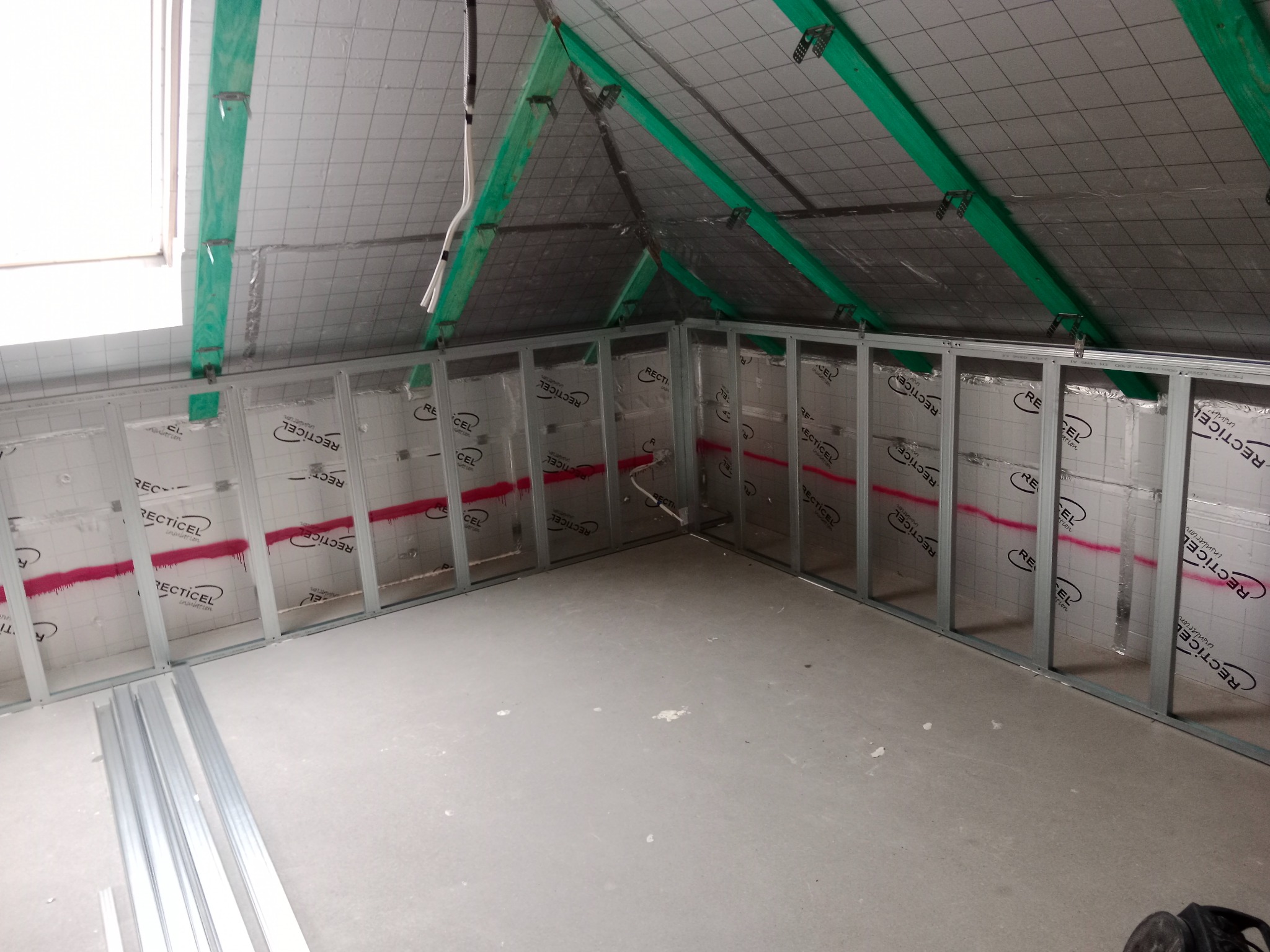 Poddasze w trakcie adaptacji: widoczne ocieplenie folią Recticel, metalowy stelaż pod płyty G-K, okno dachowe. Etap prac przed wykończeniem.