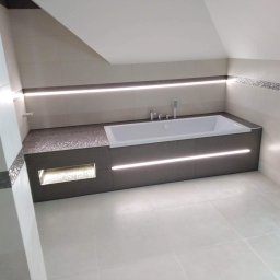 J&L Comfort - Nowoczesna łazienka na poddaszu z wanną w zabudowie z szarego kamienia, podświetleniem LED i beżowymi płytkami ceramicznymi z dekoracyjnym pasem mozaiki.