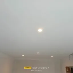 Wnętrze pokoju po malowaniu ścian i sufitu na biało, widoczne wbudowane punktowe oświetlenie sufitowe, ściany gładkie, w dolnym rogu ślady po remoncie.