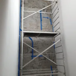 Ściana z efektem marmuru zabezpieczona folią i taśmą malarską, widoczny metalowy ruszt stojący na tle ściany.