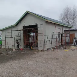 Budynek w trakcie prac elewacyjnych w Rawa Mazowiecka, widoczne rusztowania, ocieplenie, pracownicy oraz częściowo wykonany dach.