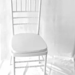 Eleganckie, białe krzesło Chiavari z miękką poduszką na siedzisku, ustawione na białym, marszczonym tle, idealne do wynajmu na uroczystości.