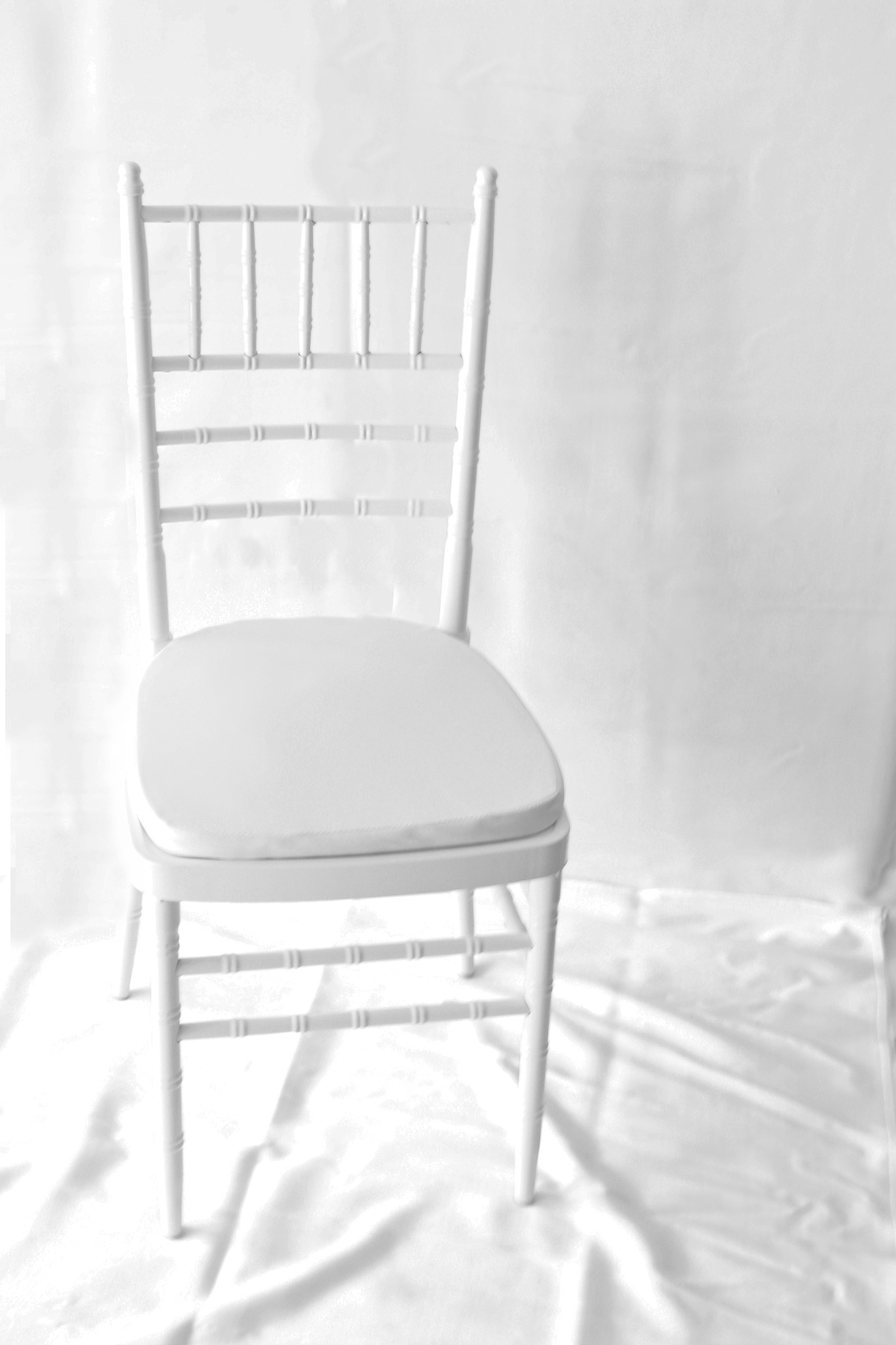 Eleganckie, białe krzesło Chiavari z miękką poduszką na siedzisku, ustawione na białym, marszczonym tle, idealne do wynajmu na uroczystości.