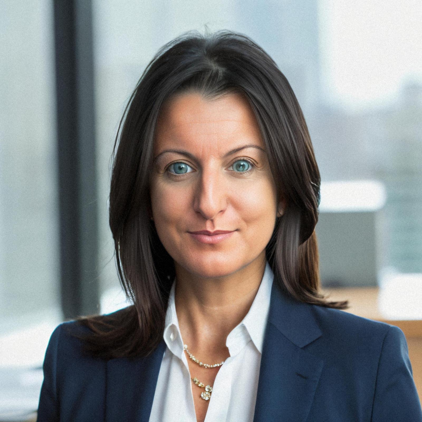 Portret kobiety w granatowej marynarce i białej koszuli, z delikatnym naszyjnikiem na tle jasnego okna. Profesjonalny wizerunek.