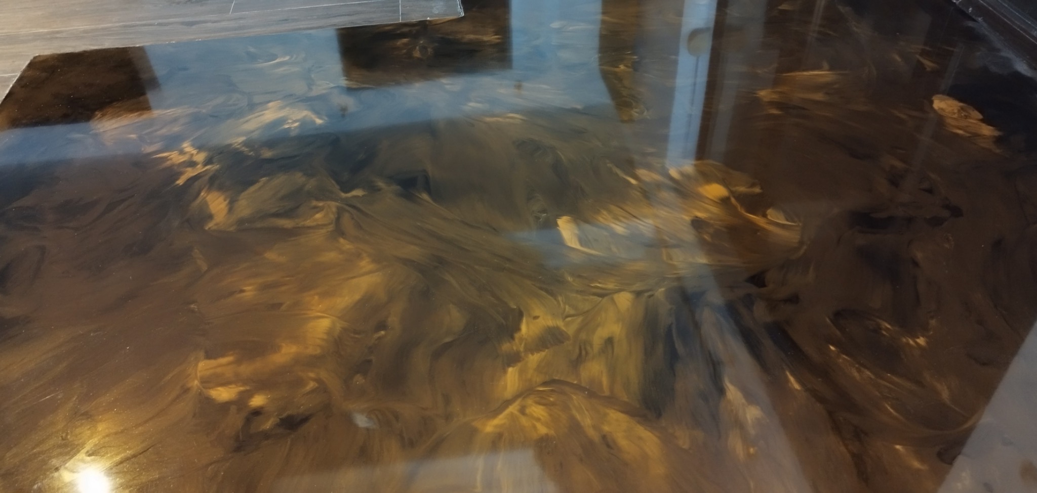 Błyszcząca, bezspoinowa podłoga w odcieniach brązu i złota, z efektem marmurkowego wzoru, odbijająca światło z okna.