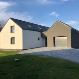 Nowoczesny dom jednorodzinny z garażem, otynkowany na biało i szaro, z ciemnym dachem i podjazdem z kostki brukowej w słoneczny dzień.