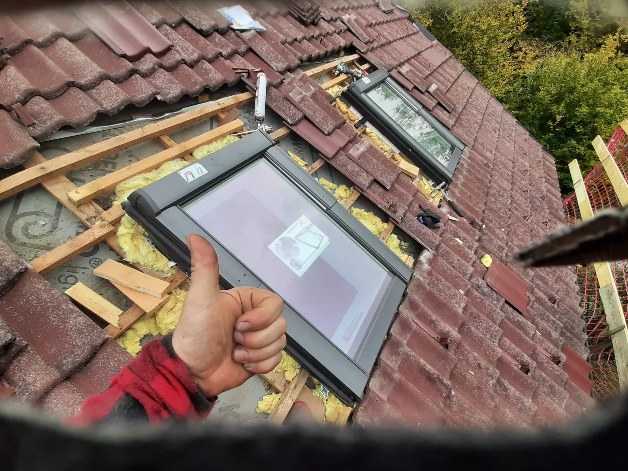 Montaż okien dachowych w trakcie realizacji, widoczna konstrukcja drewniana, izolacja z wełny mineralnej, czerwona dachówka ceramiczna, kciuk w górę w kadrze.