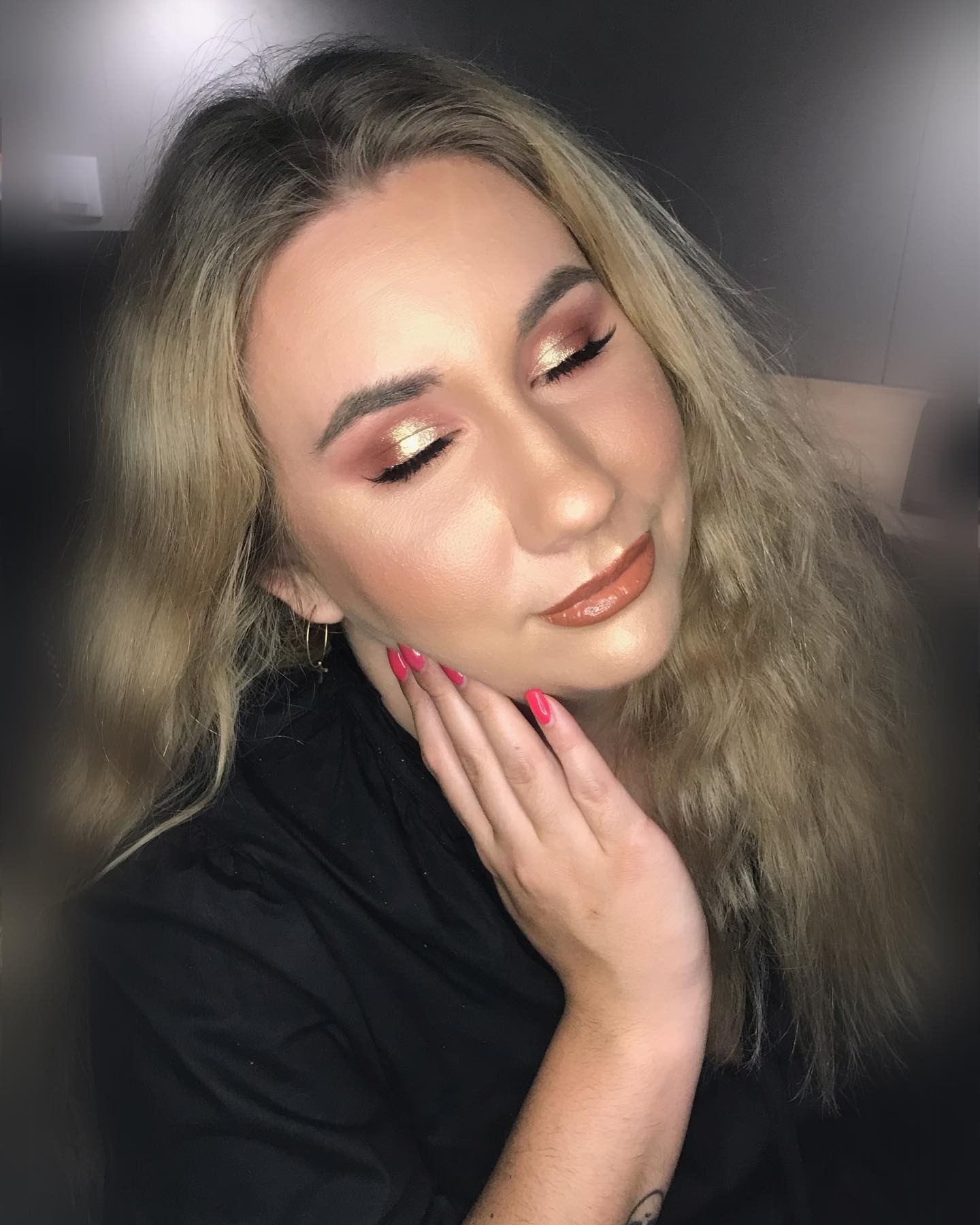 Portret kobiety z zamkniętymi oczami prezentującej ślubny look: złoty cień na powiekach, błyszczące usta w odcieniu nude i delikatny róż na policzkach. Dłoń z różowym manicure delikatnie dotyka...