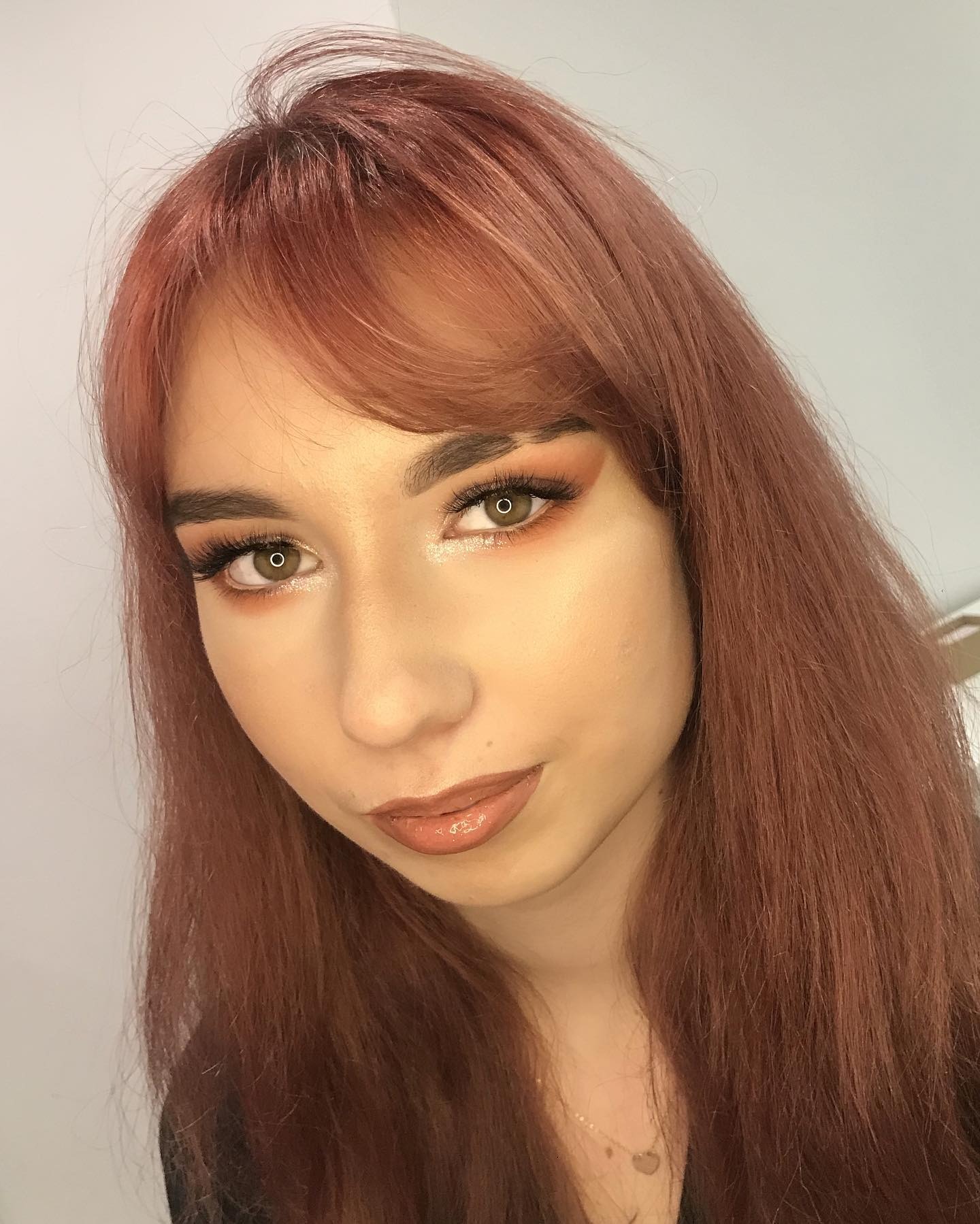 Portret kobiety z makijażem okolicznościowym w odcieniach brązu i pomarańczy, z błyszczącymi ustami i rudymi włosami z grzywką.