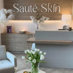 Nowoczesna zabudowa meblowa z drewnianym blatem i podświetleniem LED w salonie kosmetycznym, z dekoracjami kwiatowymi i owocami na stole.