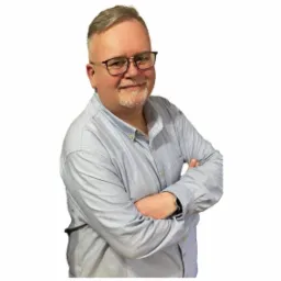 Portret uśmiechniętego mężczyzny w okularach i niebieskiej koszuli z założonymi rękami na białym tle.