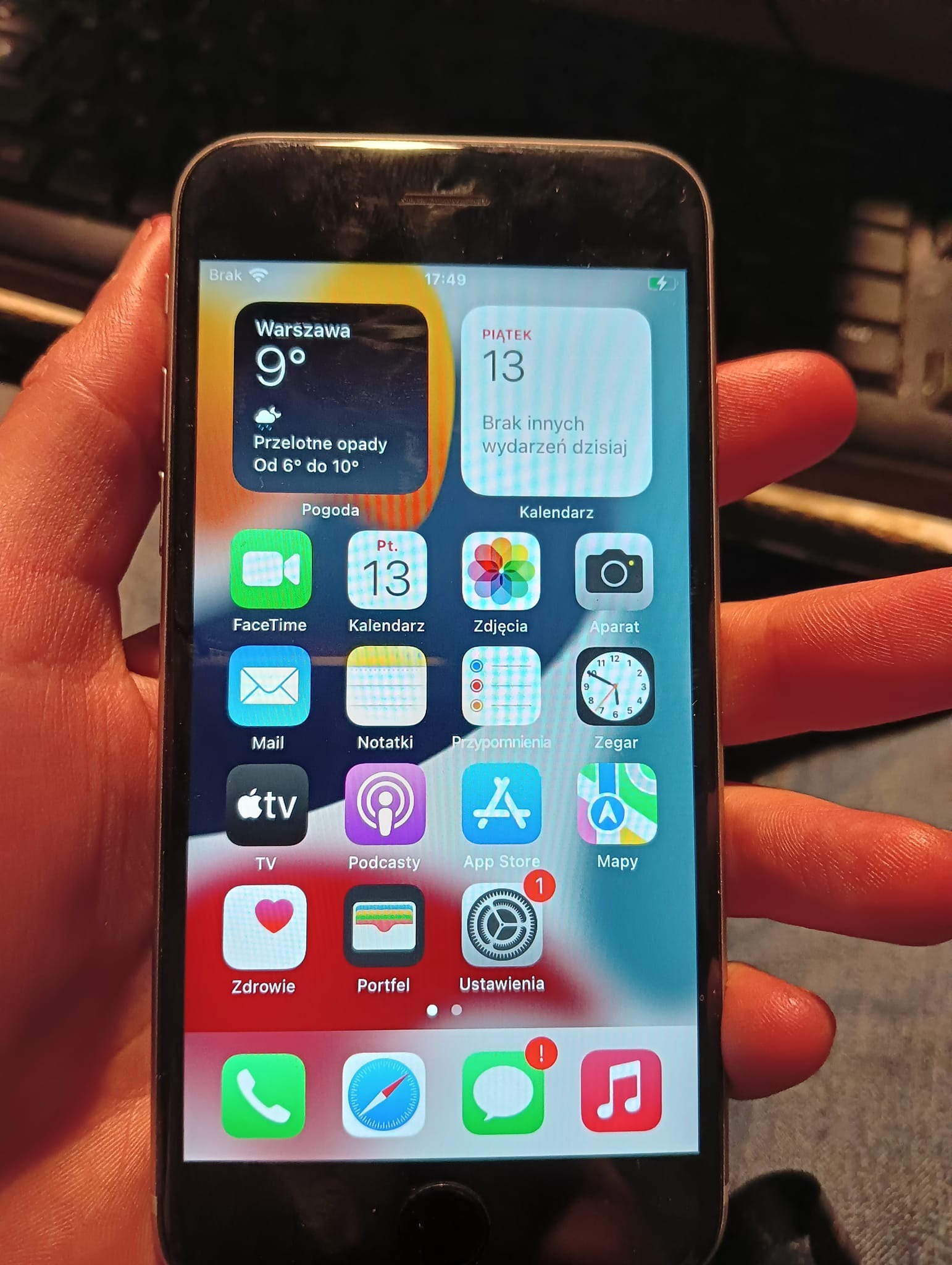 Ekran smartfona iPhone z widocznym ekranem głównym, na którym wyświetlane są ikony aplikacji, widget pogody dla Warszawy wskazujący 9 stopni Celsjusza i przelotne opady, oraz widget kalendarza...