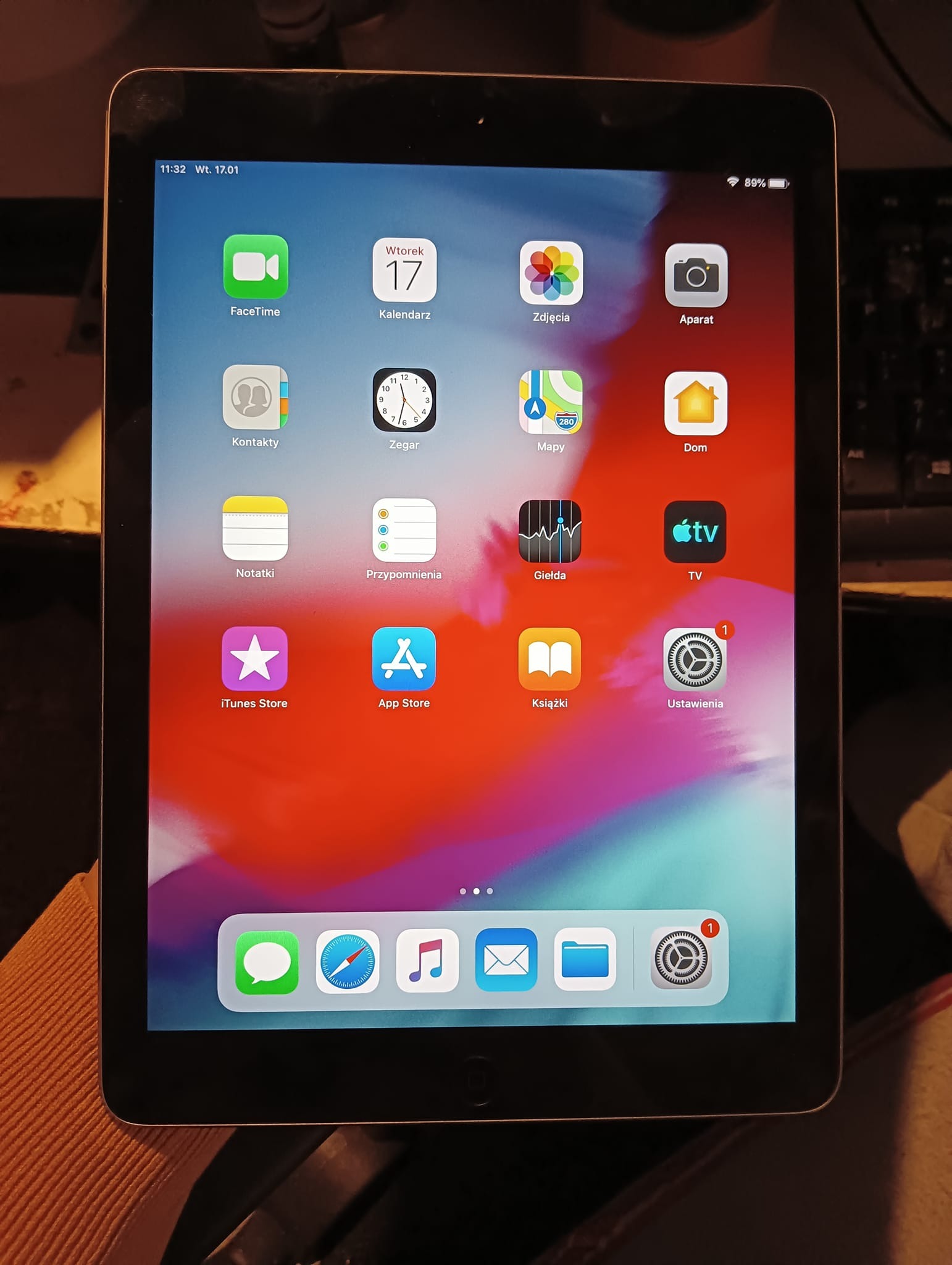 Ekran tabletu z widocznymi ikonami aplikacji, w tle fragment klawiatury i ubrania, godzina 11:32, wtorek 17 stycznia, bateria naładowana w 89%.
