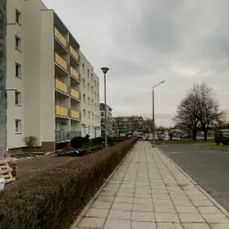 Wielopiętrowy budynek z żółtymi balkonami w trakcie ocieplania, widoczny fragment rusztowania i palety z materiałami budowlanymi na trawniku