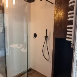 Nowoczesna łazienka z kabiną prysznicową typu walk-in, czarną armaturą, grzejnikiem drabinkowym i podłogą z blachy ryflowanej.