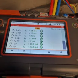 Miernik elektryczny MPI-540 z kolorowymi przewodami pomiarowymi (czerwony, ż&oacute;łty, niebieski) wyświetlający wyniki pomiar&oacute;w parametr&oacute;w RCD, w tym czasy zadziałania i prądy wyzwalania.