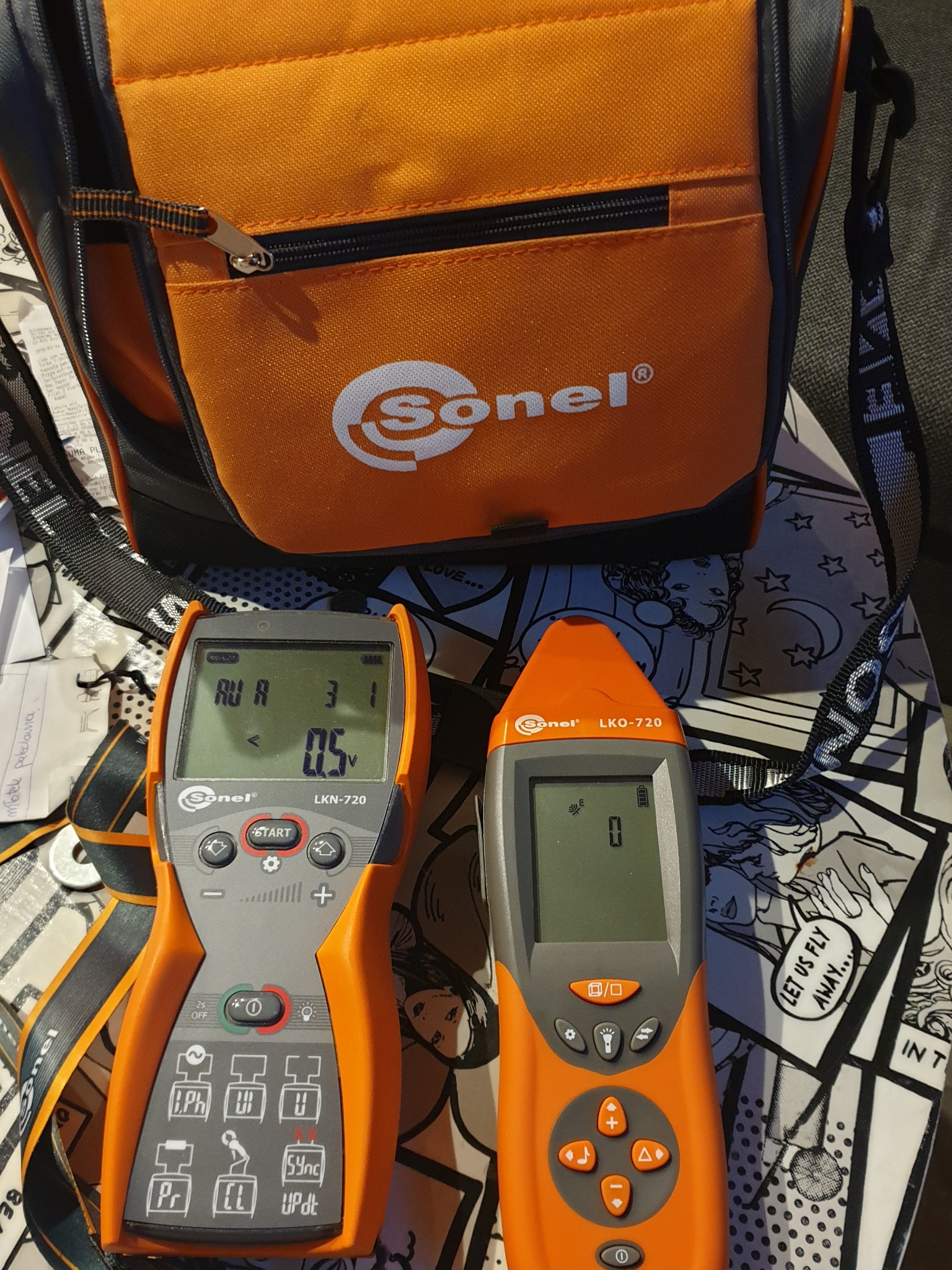 Dwa lokalizatory przewodów Sonel LKN-720 i LKO-720, leżące obok torby narzędziowej Sonel, na tle stolika z komiksowym wzorem.