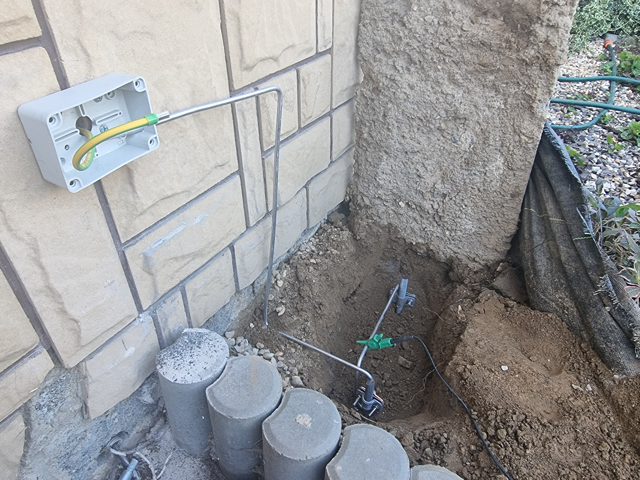 Uziemienie pionowe i poziome w trakcie montażu przy budynku z kamienia w Rzeszowie. Widoczna puszka instalacyjna, przewód ochronny żółto-zielony oraz elementy uziomu w wykopie.