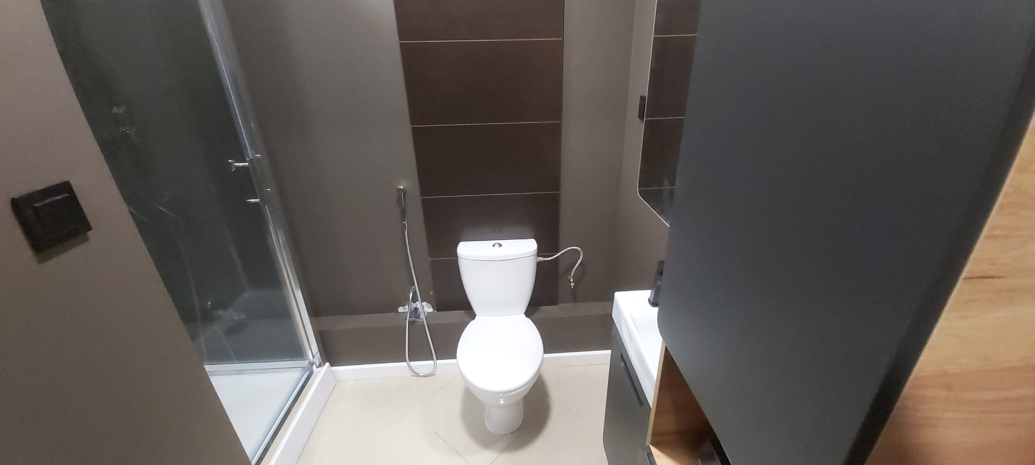 Wykończona łazienka z kabiną prysznicową, toaletą z bidetką, umywalką z szafką w odcieniach szarości i brązu, widok z perspektywy drzwi.