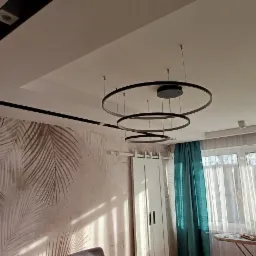 Nowoczesne wnętrze: Sufit podwieszany z czarnym kanałem oświetleniowym, tapeta z motywem liści palmowych, okrągła lampa wisząca, białe przesuwne drzwi i turkusowe zasłony przy oknie.