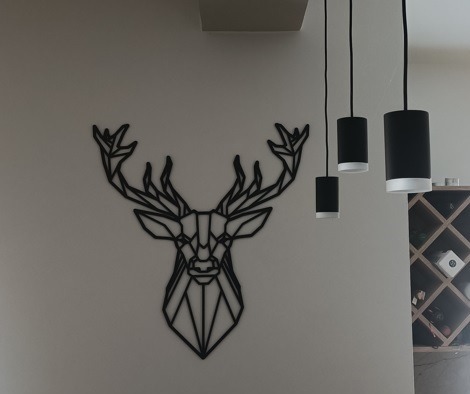 Geometryczny wizerunek głowy jelenia jako dekoracja ścienna, oświetlony przez cztery cylindryczne lampy wiszące z czarnymi kloszami i białymi akcentami, obok regału na wino.