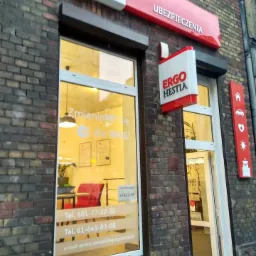 Fasada biura Ergo Hestia z szyldami reklamowymi, widoczne numery telefonów i adres e-mail na witrynie, budynek z cegły.