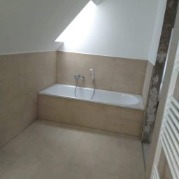 Natalii kuzyna - Łazienka w trakcie remontu, widoczna wanna obudowana płytkami w odcieniach beżu, fragment grzejnika drabinkowego i sufit ze skosem oraz okno dachowe, ściana przy drzwiach w trakcie wykończenia.