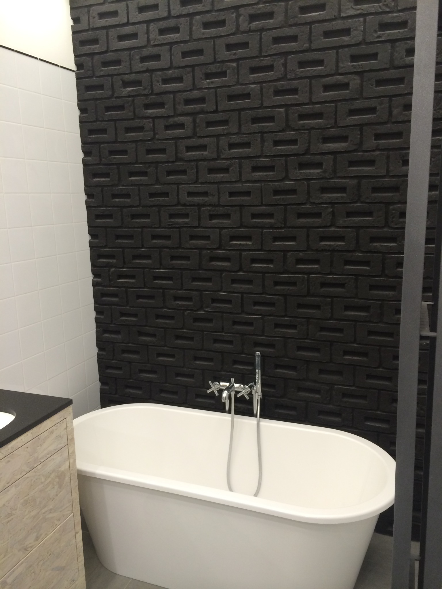 Biała wolnostojąca wanna na tle ściany z czarnej cegły w nowoczesnej łazience.