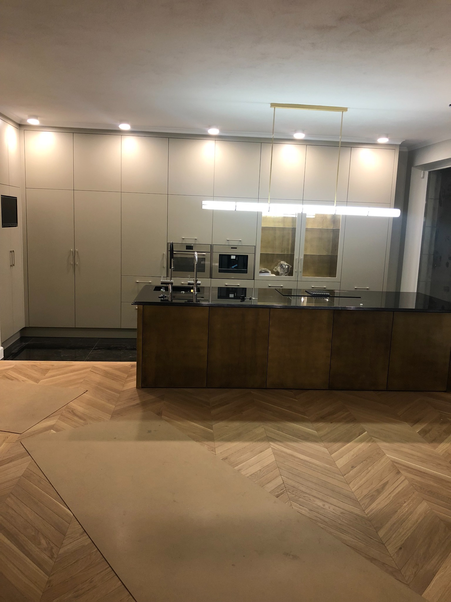 Nowoczesna kuchnia z wyspą i parkietem w jodełkę, zabezpieczonym kartonem podczas prac wykończeniowych.