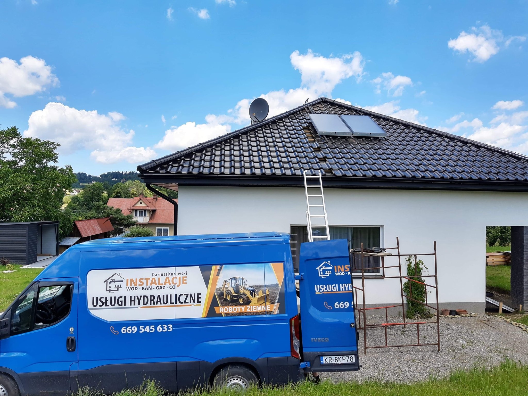 Niebieski samochód dostawczy z reklamą usług hydraulicznych na tle domu z panelami słonecznymi na dachu i rozstawioną drabiną.