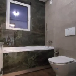 Nowoczesna łazienka z wanną obudowaną zielonym marmurem, umywalką nablatową i pralką LG. Minimalistyczny design, szare płytki, biała armatura i okno.