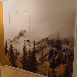 LEM-ART Remonty i Wykończenia Wnętrz Piotr Lemański - Pokój z fototapetą górskiego lasu na ścianie i ukrytymi drzwiami. Jasna podłoga z paneli. Minimalistyczny design, ciepłe oświetlenie.