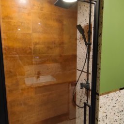 LEM-ART Remonty i Wykończenia Wnętrz Piotr Lemański - Kabina prysznicowa z czarnymi profilami, brązowe płytki imitujące kamień na ścianie i posadzka lastryko. Widoczna bateria prysznicowa i umywalka.