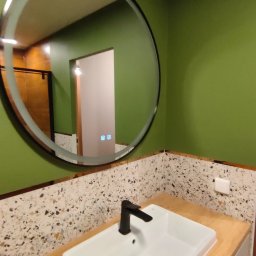 LEM-ART Remonty i Wykończenia Wnętrz Piotr Lemański - Nowoczesna łazienka z zielonymi ścianami, okrągłym lustrem z podświetleniem i umywalką nablatową z czarną armaturą. Blat drewnopodobny, ściana wykończona mozaiką.