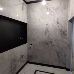 LEM-ART Remonty i Wykończenia Wnętrz Piotr Lemański - Wykończona łazienka z marmurowymi płytkami, czarnymi akcentami i wiszącą toaletą. Widoczne instalacje wodne i oświetlenie sufitowe.