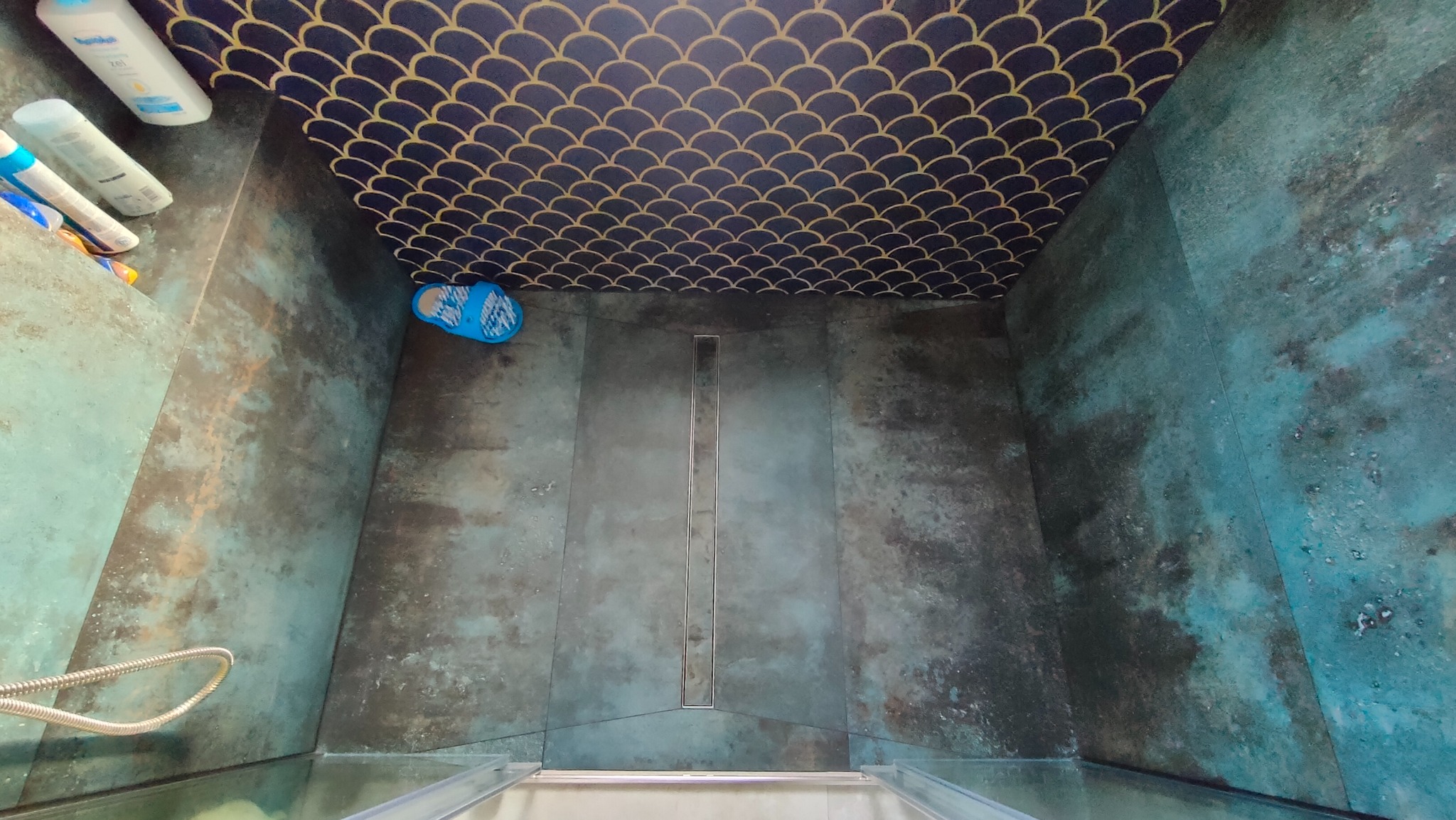 Nowoczesna kabina prysznicowa z odpływem liniowym, wykończona płytkami w odcieniach turkusu i złota, z dekoracyjnym wzorem rybiej łuski na suficie.