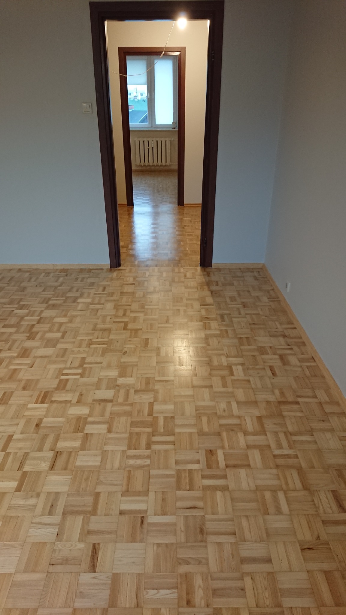 Parkiet ułożony w jodełkę na podłodze w pustym pokoju, widok przez otwarte drzwi do kolejnych pomieszczeń.