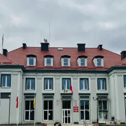 Budynek Starostwa Powiatowego z nową, czerwoną dachówką, widoczne okna dachowe i kominy, na elewacji powiewają flagi Polski i Ukrainy.